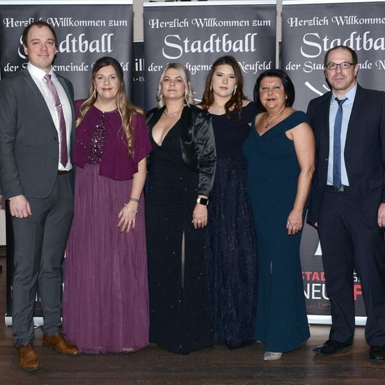Eine Gruppe von sechs Personen steht vor Bannern für Stadtball. Sie lächeln alle und sind formell gekleidet.