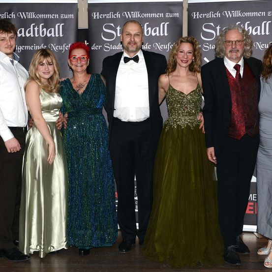 Eine Gruppe von Menschen in formeller Kleidung posiert für ein Foto. Sie stehen vor einem Hintergrund mit Text auf Deutsch.