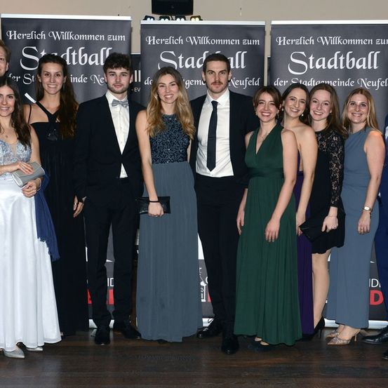 Eine Gruppe von Menschen steht für ein Foto bei einem Stadtball-Event, mit Bannern dahinter, die Herzlich Willkommen zum Stadtball sagen.