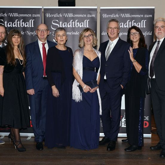 Eine Gruppe von Menschen in formeller Kleidung posiert für ein Foto vor einem Hintergrund mit einem Stadtlogo.