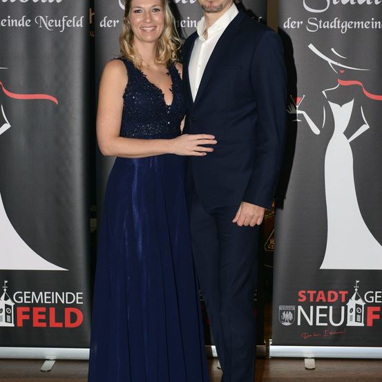 Ein Mann und eine Frau in formeller Kleidung posieren für ein Foto vor einem Schild.