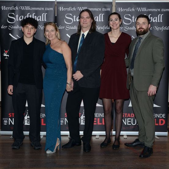 Eine Gruppe von Menschen posiert für ein Foto vor einem schwarzen Banner mit weißem Text, wahrscheinlich bei einer Veranstaltung.