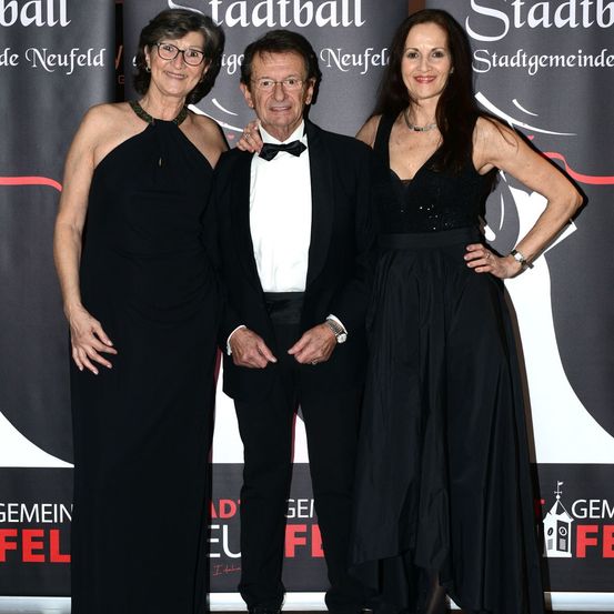 Drei Menschen in schwarzer Abendkleidung stehen zusammen, lächeln und posieren für ein Foto auf der Bühne.