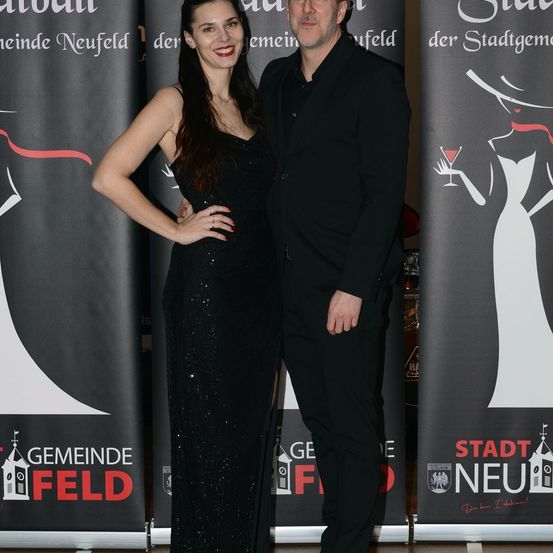 Eine Frau und ein Mann stehen nebeneinander vor einem Banner mit den Worten Gemeinde Neufeld.