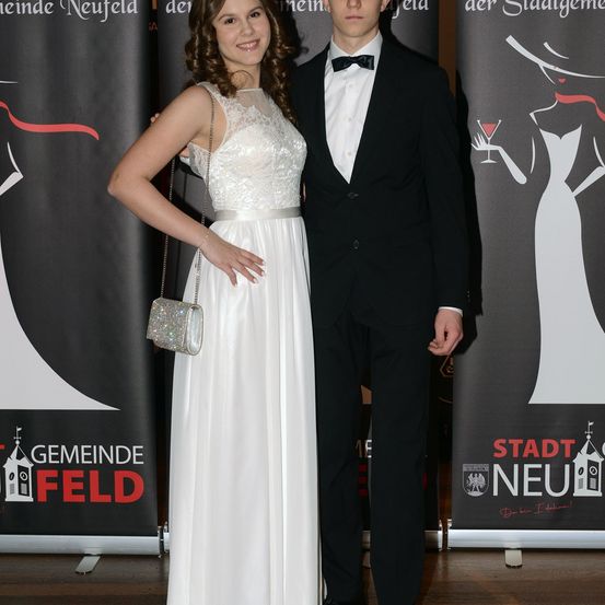 Ein Mann und eine Frau in formeller Kleidung stehen gemeinsam vor einem Hintergrund, auf dem 'Gemeinde Neufeld' und 'Stadt Neufeld' beworben werden.