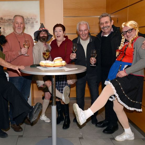 Eine Gruppe von Menschen in Kostümen versammelt sich um einen Tisch mit Weinläsern und Gebäck und posiert für ein Foto.