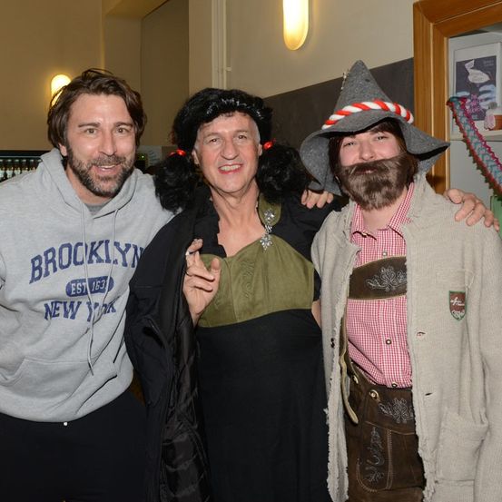 Drei Personen posieren für ein Foto, darunter ein Mann in einem Brooklyn-Hoodie, eine Frau in einer Hexen-Kostüm und ein Mann in traditioneller deutscher Kleidung.