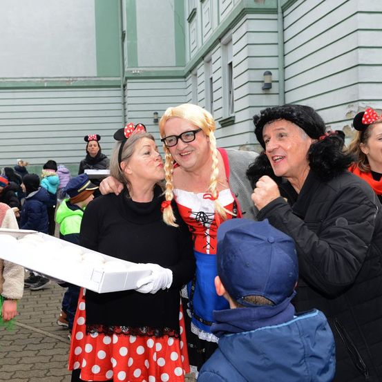 Eine Gruppe von Erwachsenen und Kindern in verschiedenen Kostümen, einer hält eine Schale mit Donuts. Sie lächeln und scheinen für ein Foto zu posieren.