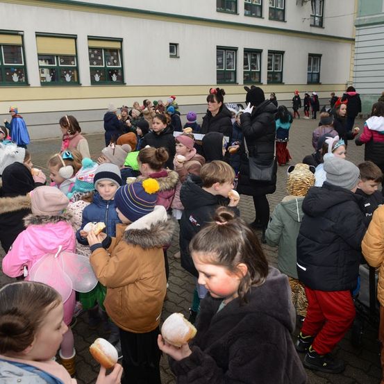 Eine Gruppe von Kindern in Kostümen isst Donuts draußen vor einem Gebäude.