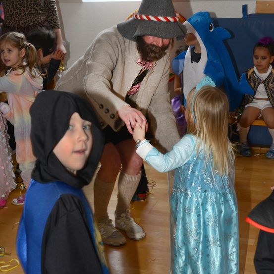 Ein Mann in einem Piratenkostüm tanzt mit einem kleinen Mädchen, das Elsa darstellt. Andere Kinder in verschiedenen Kostümen beobachten. Der Raum ist für einen festlichen Anlass geschmückt.