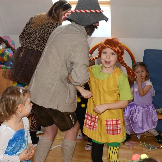 Eine Gruppe von Kindern in Kostümen, ein Mädchen in einem grünen Kleid, ein Mann in einem Kostüm und andere spielen.