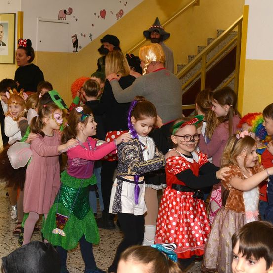 Eine Gruppe von Kindern in verschiedenen Kostümen tanzt in einem Flur. Ein Mann in einem Piratenkostüm steht in der Nähe der Treppe.