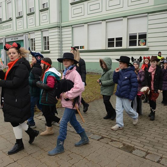 Eine Gruppe von Menschen in Kostümen geht auf einem gepflasterten Weg. Die Frau vorne trägt Minnie Mouse Ohren. Hinter ihr ist eine Frau, die einen Stock hält. Die Frau vorne trägt Stiefel.