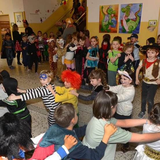 Eine große Gruppe von Kindern, einige in Kostümen, stehen im Kreis und halten sich an den Händen. Sie scheinen an einem Halloween-Event teilzunehmen.