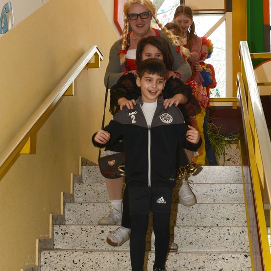Ein Junge mit der Nummer 2 auf seiner Jacke steigt die Treppe hinauf, unterstützt von einer Frau und zwei Mädchen, von denen eines einen Clown hält.