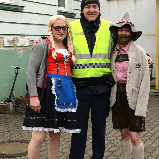 Drei Personen in traditioneller deutscher Kleidung, wobei ein Polizist in einem gelben Weste zwischen einem Mann und einer Frau steht. Sie posieren für ein Foto.