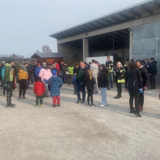Eine Gruppe von Menschen steht draußen vor einem Gebäude. Einige sind in Jacken gekleidet und andere in Mützen. Einige tragen Rucksäcke.