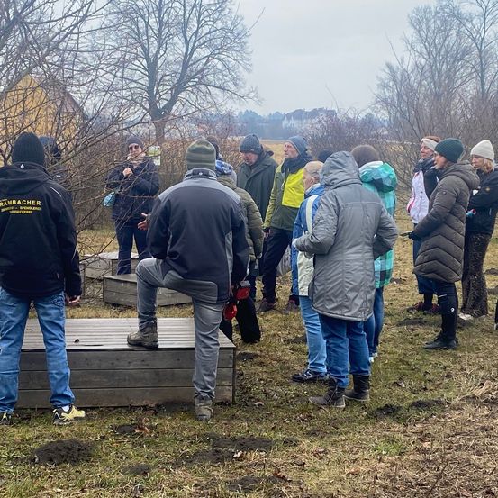 Eine Gruppe von Menschen in Winterkleidung versammelt sich in einem Außenbereich, möglicherweise für ein Workshop, einige stehen auf Holzplattformen.