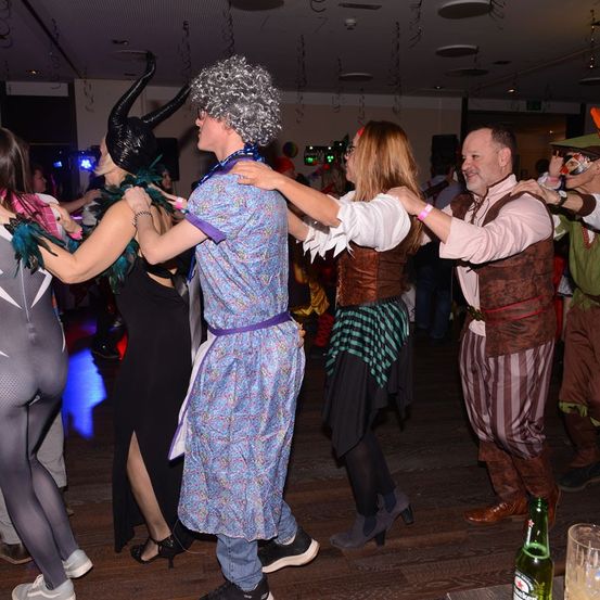 Mehrere Menschen tanzen in einem Club. Ein Mann ist als Teufel verkleidet. Die Frau neben ihm trägt ein mittelalterliches Kostüm.