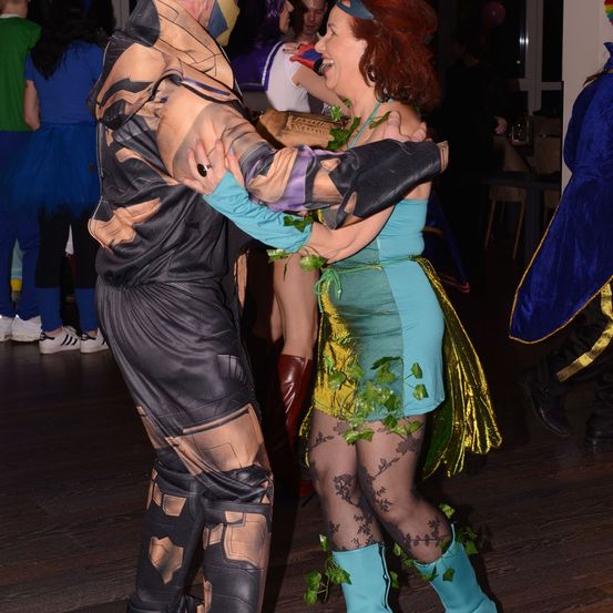 Ein Mann in einem Kostüm tanzt eng mit einer Frau in einem grünen Kostüm mit Blättern, auf einer Party.