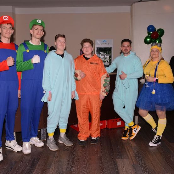 Eine Gruppe von Menschen in Kostümen posiert für ein Foto mit einem Coca-Cola-Kühlschrank im Hintergrund.