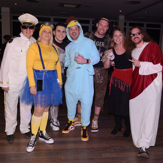 Eine Gruppe von Menschen in verschiedenen Kostümen posiert für ein Foto in Innenräumen, darunter ein Kapitän, ein gelber Charakter und ein Jesus-Kostüm.