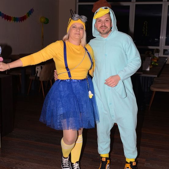 Ein Mann und eine Frau in Kostümen, wahrscheinlich für eine Party, posieren für ein Foto mit Möbeln und Dekorationen im Hintergrund.