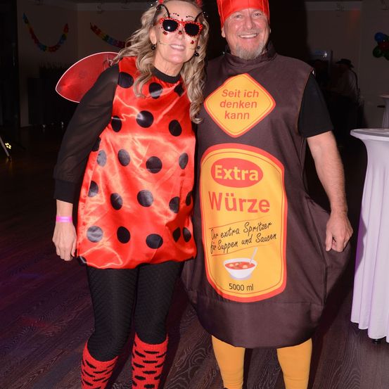 Ein Mann und eine Frau in Kostümen, er in einer Gewürzflasche, sie in einem Marienkäfer-Kostüm, stehen auf einer Tanzfläche.