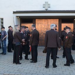 Eine Gruppe von Menschen in Uniformen steht vor einem Gebäude. Sie scheinen miteinander zu sprechen. Einige tragen Hüte und Schuhe. Ein Kreuz ist über dem Gebäude montiert.