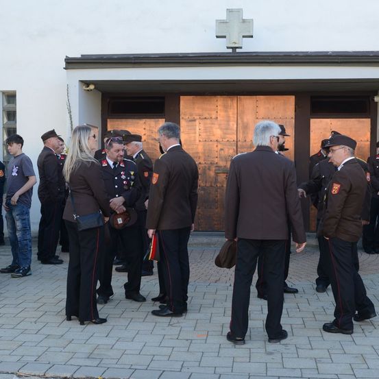 Eine Gruppe von Menschen in Uniformen steht vor einem Gebäude. Sie scheinen miteinander zu sprechen. Einige tragen Hüte und Schuhe. Ein Kreuz ist über dem Gebäude montiert.