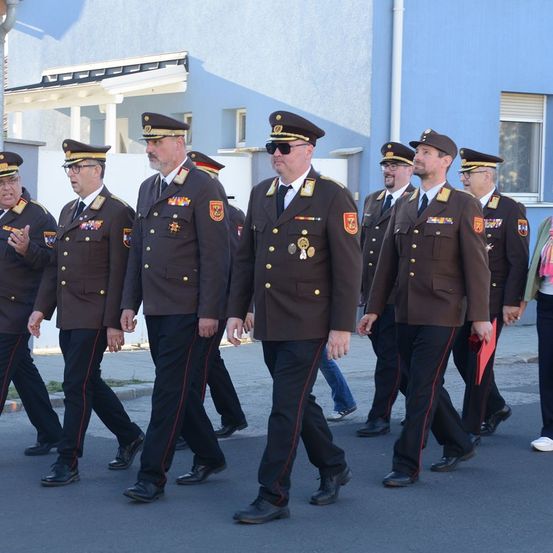 Eine Gruppe von Militäroffizieren in Uniform, die bei einer Parade gehen und Hüte und Brillen tragen. Sie marschieren in einer Reihe, möglicherweise bei einer zeremoniellen Veranstaltung.