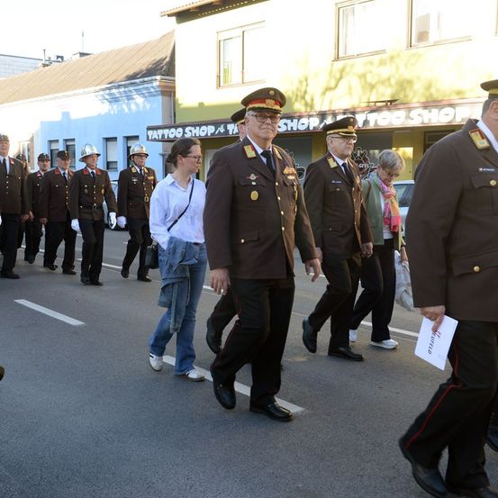 Eine Gruppe von Militäroffizieren in Uniform geht die Straße entlang, begleitet von einem Zivilisten. Die Szene spielt vor einem Tattoo-Shop.