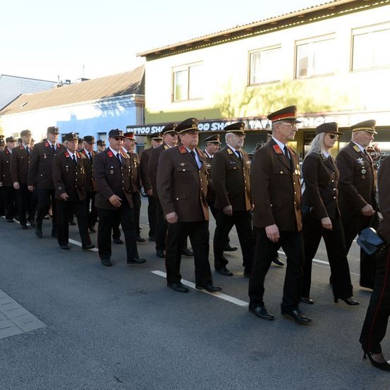 Eine Reihe von Menschen in Militäruniformen geht eine Straße entlang. Sie nehmen an einer Parade teil.
