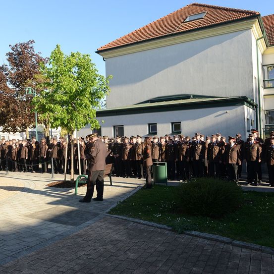 Eine Gruppe uniformierter Personen steht in Formation vor einem Gebäude mit roten Dachziegeln.