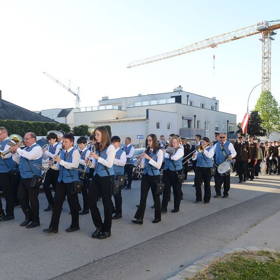 Eine Blaskapelle spielt auf einer Stadtstraße, mit Gebäuden und einem Baukran im Hintergrund.
