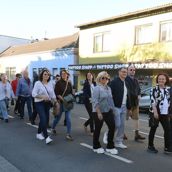 Eine Gruppe von Menschen geht auf der Straße mit einem Tattoo-Shop an der Seite. Sie tragen alle Sonnenbrillen und einige sind in Turnschuhen. Ein Auto ist vor dem Shop geparkt.