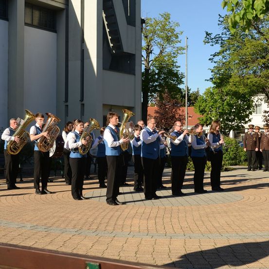 Eine Gruppe von Musikern in blauen Westen spielt Blechblasinstrumente auf einem gepflasterten Platz vor einem Gebäude.