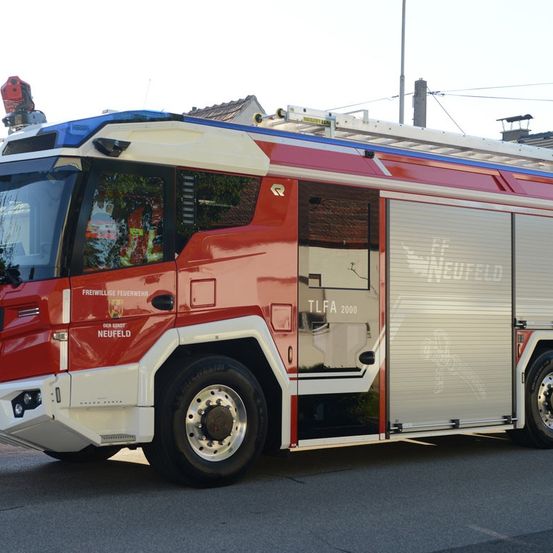 Ein rot-weißer Feuerwehrwagen mit einer Leiter auf dem Dach steht am Straßenrand.
