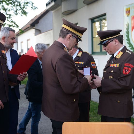 Mehrere Militäroffiziere in braunen Uniformen stehen in einer formellen Umgebung, wobei ein Offizier einem anderen eine Medaille überreicht.