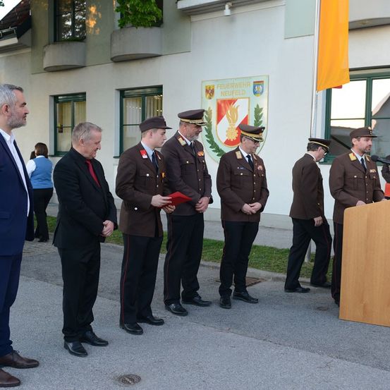 Fünf Militäroffiziere stehen in Uniform vor einem Gebäude. Ein Mann mit einem Mikrofon steht vor ihnen.