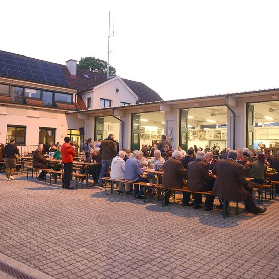 Men sitzen an Tischen vor einem Gebäude mit Solarzellen auf einem Ziegelsteinpflaster.