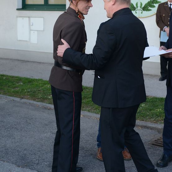 Ein Mann in Uniform und ein Mann im Anzug unterhalten sich auf der Straße vor einem Gebäude.