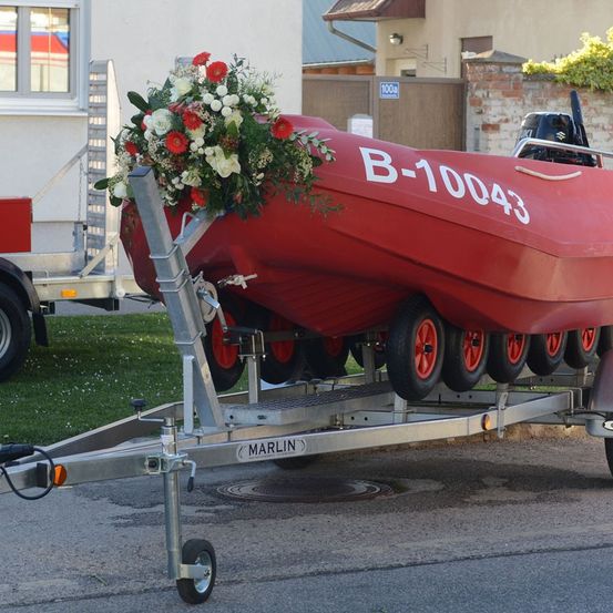 Ein rotes Boot mit der Nummer B-10043 steht auf einem Anhänger mit Blumen vorne.