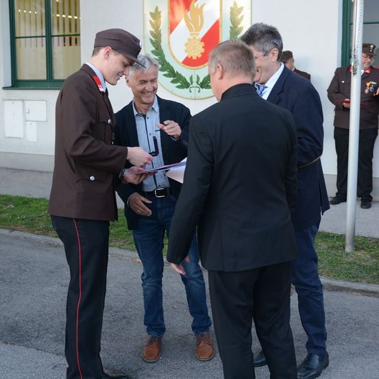 Ein uniformierter Mann übergibt einem lächelnden Mann in einem Anzug ein Blatt Papier, umgeben von drei anderen auf der Straße.