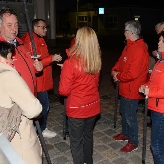 Eine Gruppe von Menschen in roten Jacken steht bei Nacht draußen, wahrscheinlich auf einer Tour, wobei eine Person ein Schwert hält.