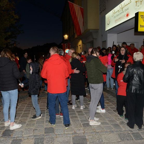 Eine Gruppe von Menschen in Rot steht bei Nacht vor einem Gebäude, einige halten Kerzen.