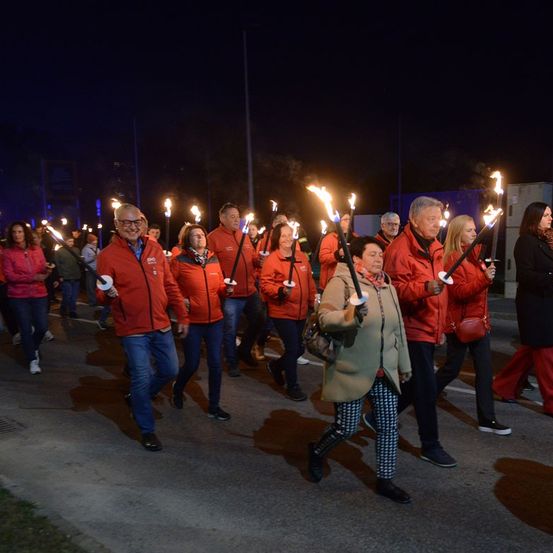 Eine Gruppe von Menschen in roten Jacken und mit brennenden Fackeln geht bei Nacht eine Straße entlang.