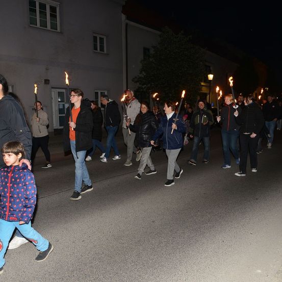 Eine Gruppe von Menschen geht bei Nacht die Straße entlang und hält brennende Fackeln. Sie sind in Winterkleidung gekleidet.