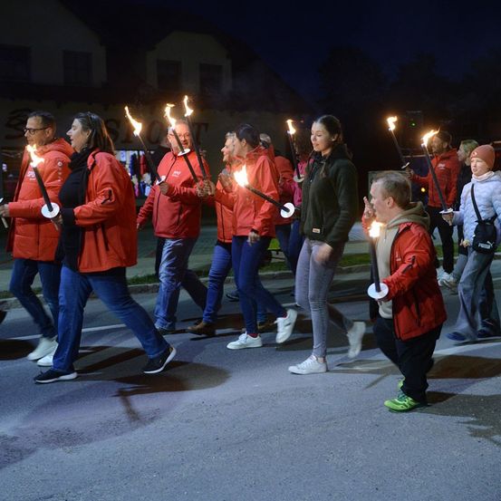 Eine Gruppe von Menschen in roten Jacken geht bei Nacht die Straße entlang und hält brennende Fackeln. Sie nehmen an einer Fackelprozession teil.