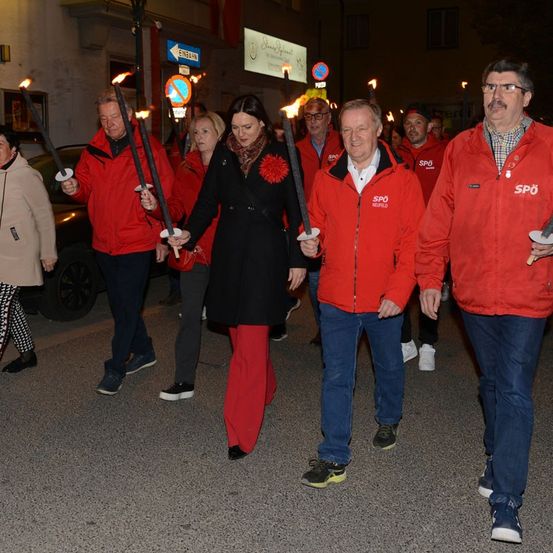 Eine Gruppe von Menschen in roten Jacken und mit brennenden Fackeln in der Hand geht bei Nacht auf einer Prozession.